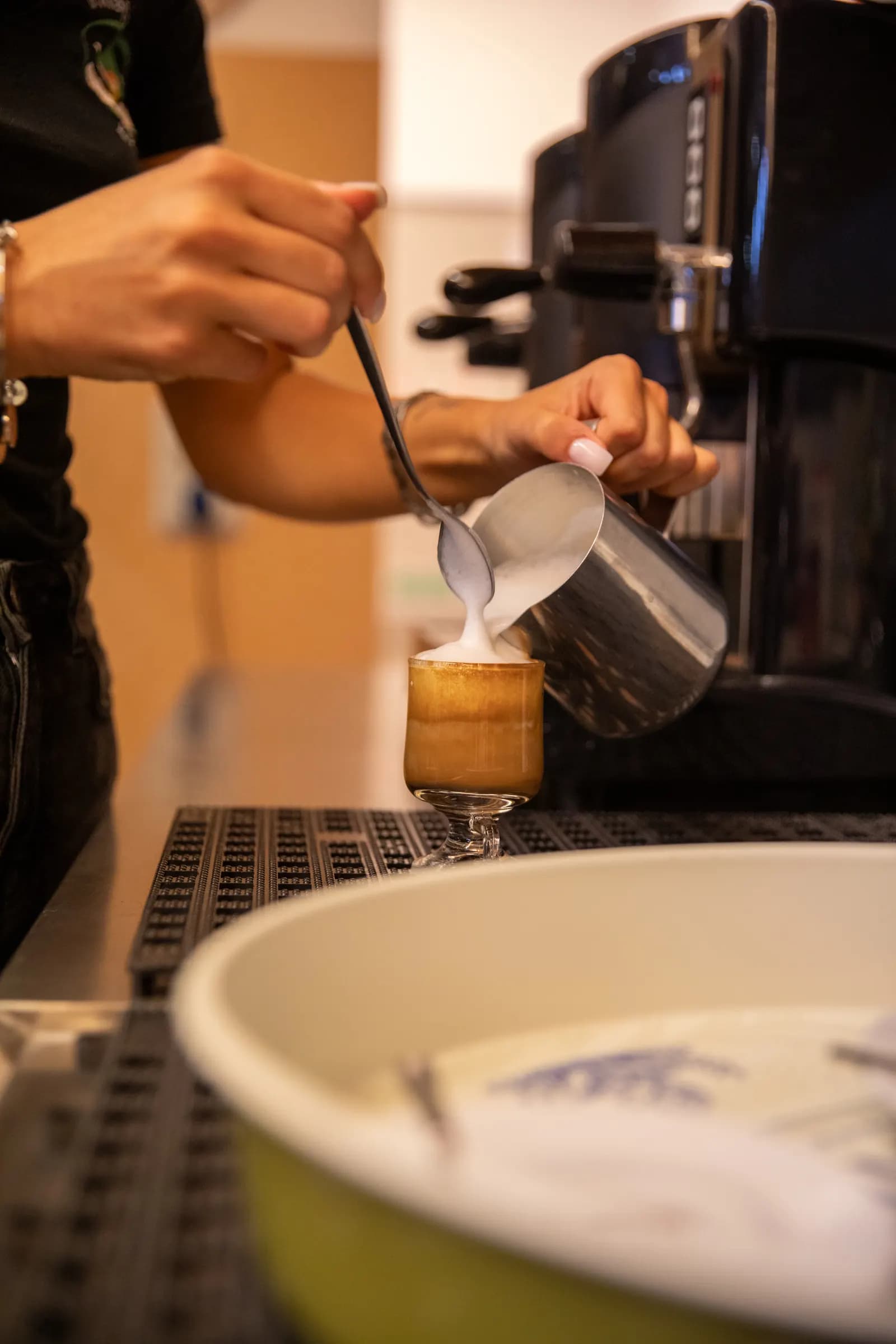 Le mani di una barista versano il latte in un bicchiere al banco del bar