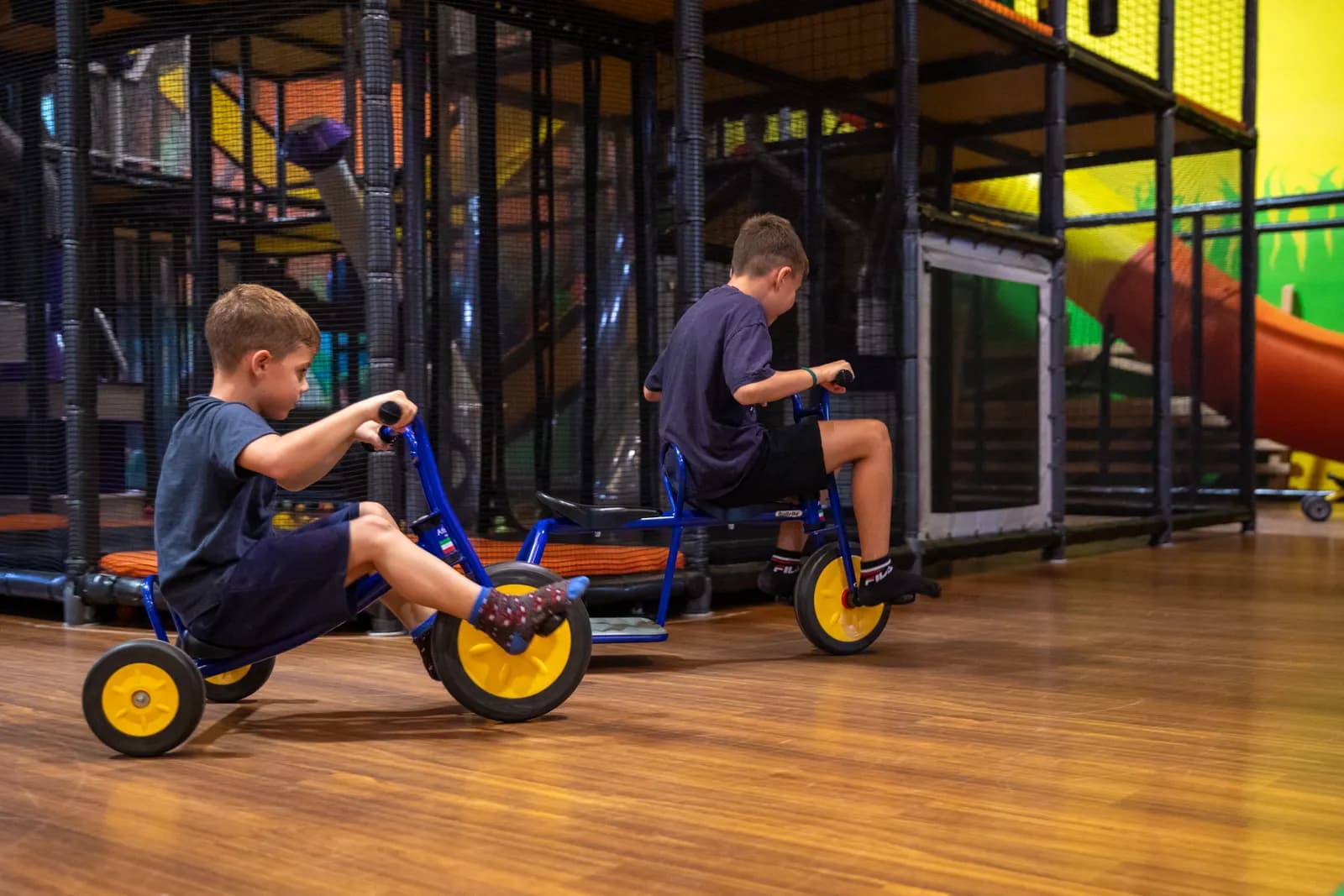 Due bambini pedalano sui tricicli lungo il circuito di legno