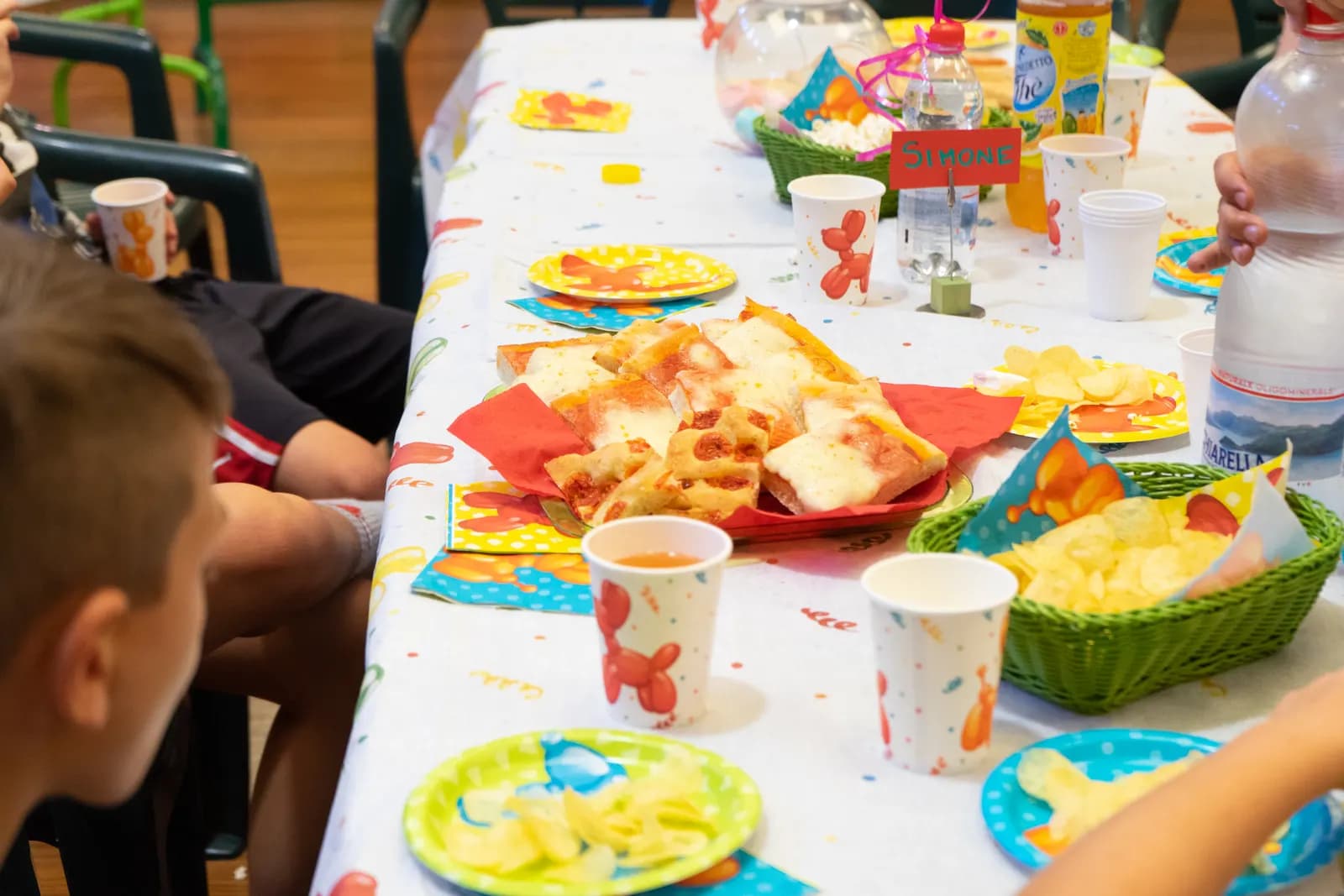Tavolata vista per lungo con pizza, patatine e bicchieri colorati