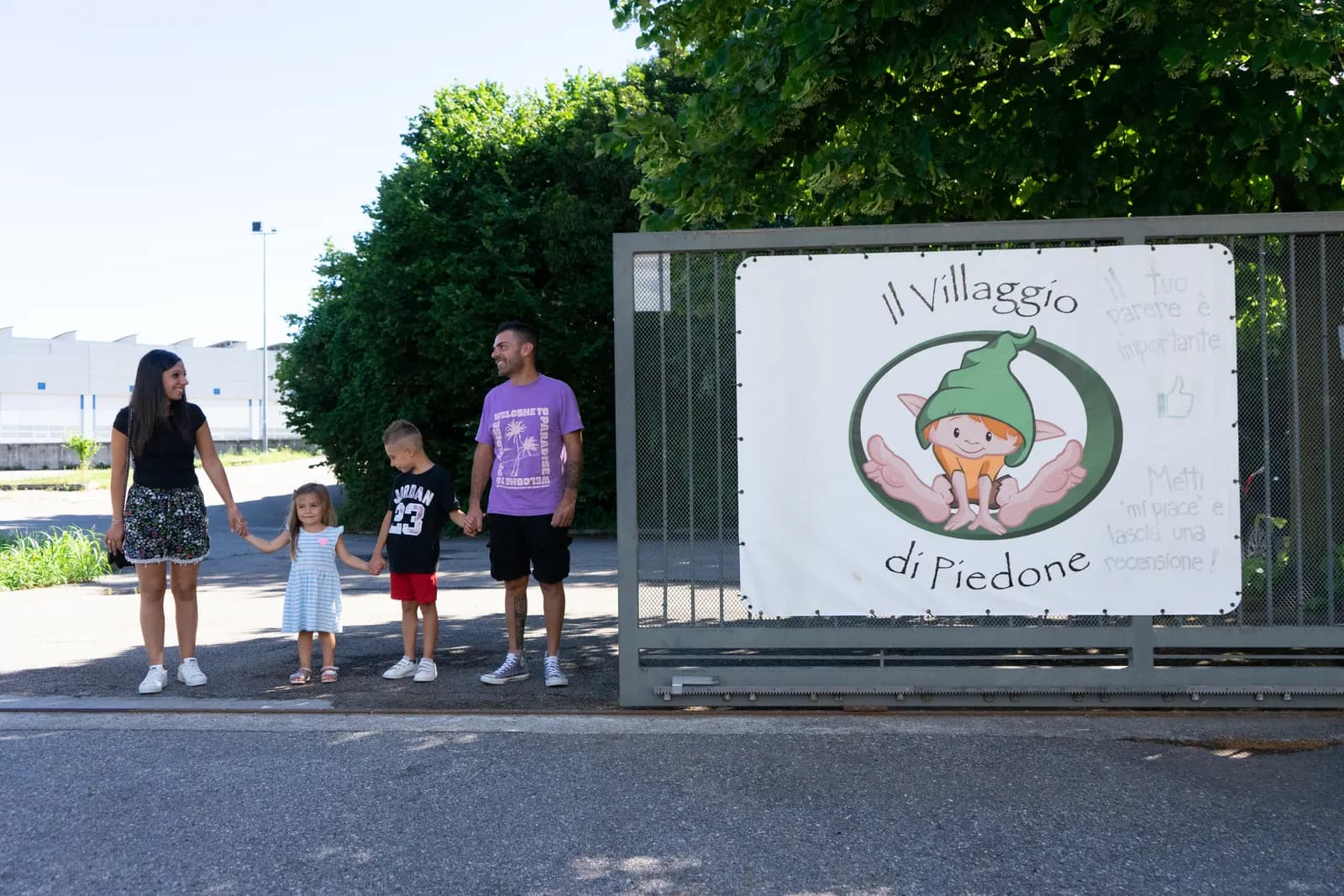 Una famiglia arriva a piedi davanti all'insegna del Villaggio di Piedone